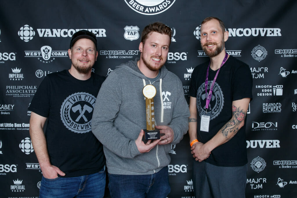 photo of three men with middle holding trophy for Best in Show awarded to Twin City Brewing at 2018 BC Beer Awards ceremony