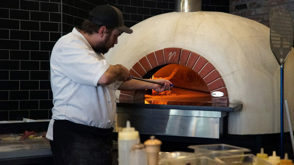 image of man putting pizza in wood-fired oven at CrossRoads Brewing in Prince George, BC