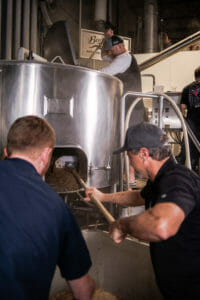 men taking spent grain out of barrel