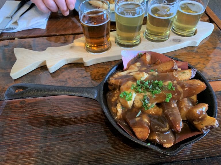 image of Provisions Kitchen's hand cut Russet fries poutine in foreground, with beer flight from Kettle River in background