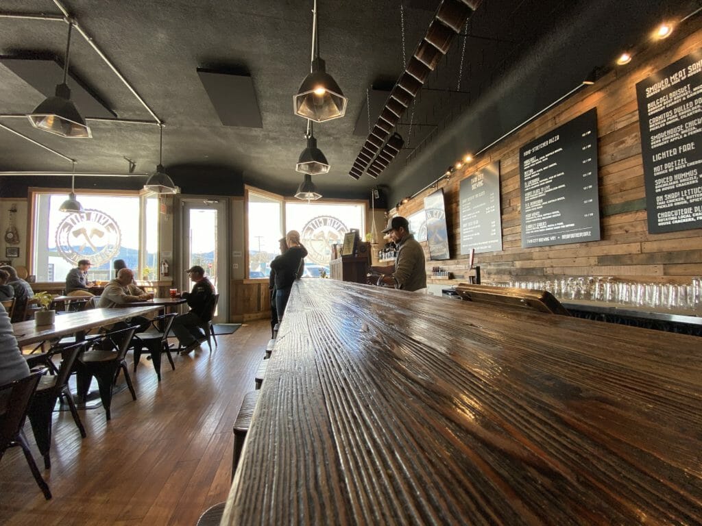 image of long wooden table with people in background enjoying the inside of Twin City Brewing's tasting room in Port Alberni