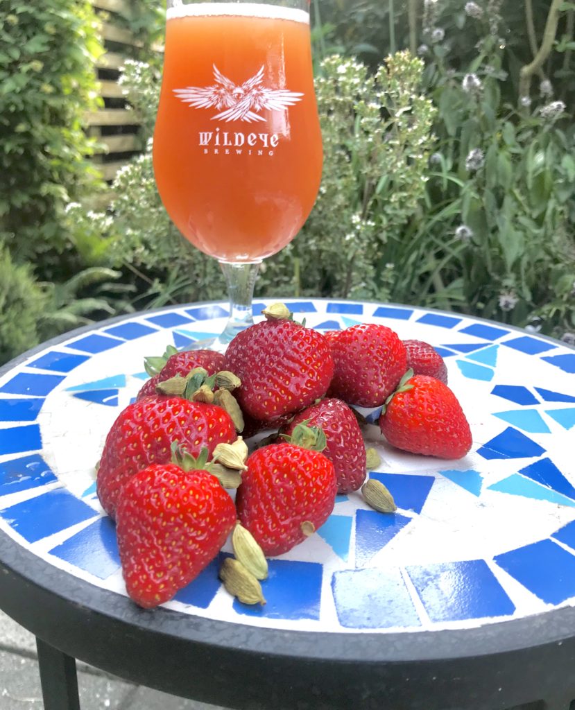 photo of Wildeye Brewing's spring beer release of the Strawberry Cardamom Gose and a bunch of fresh strawberries on a patio table