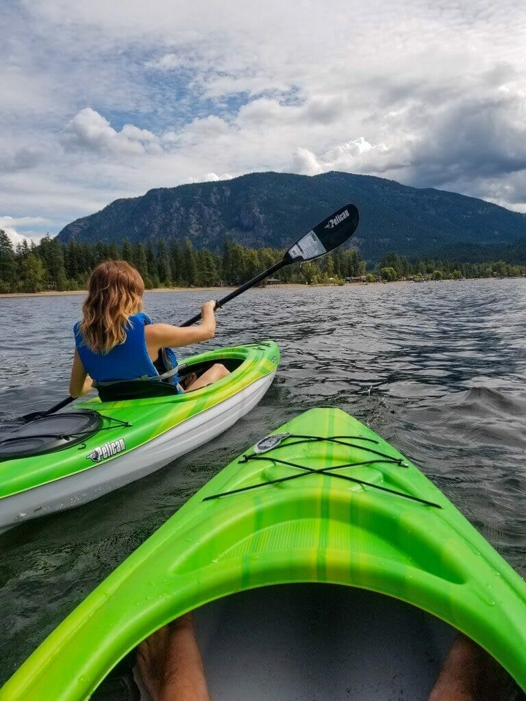 Photo of front of a kayak on Little Shuswap Lake, with a woman in another kayak to the left paddling.