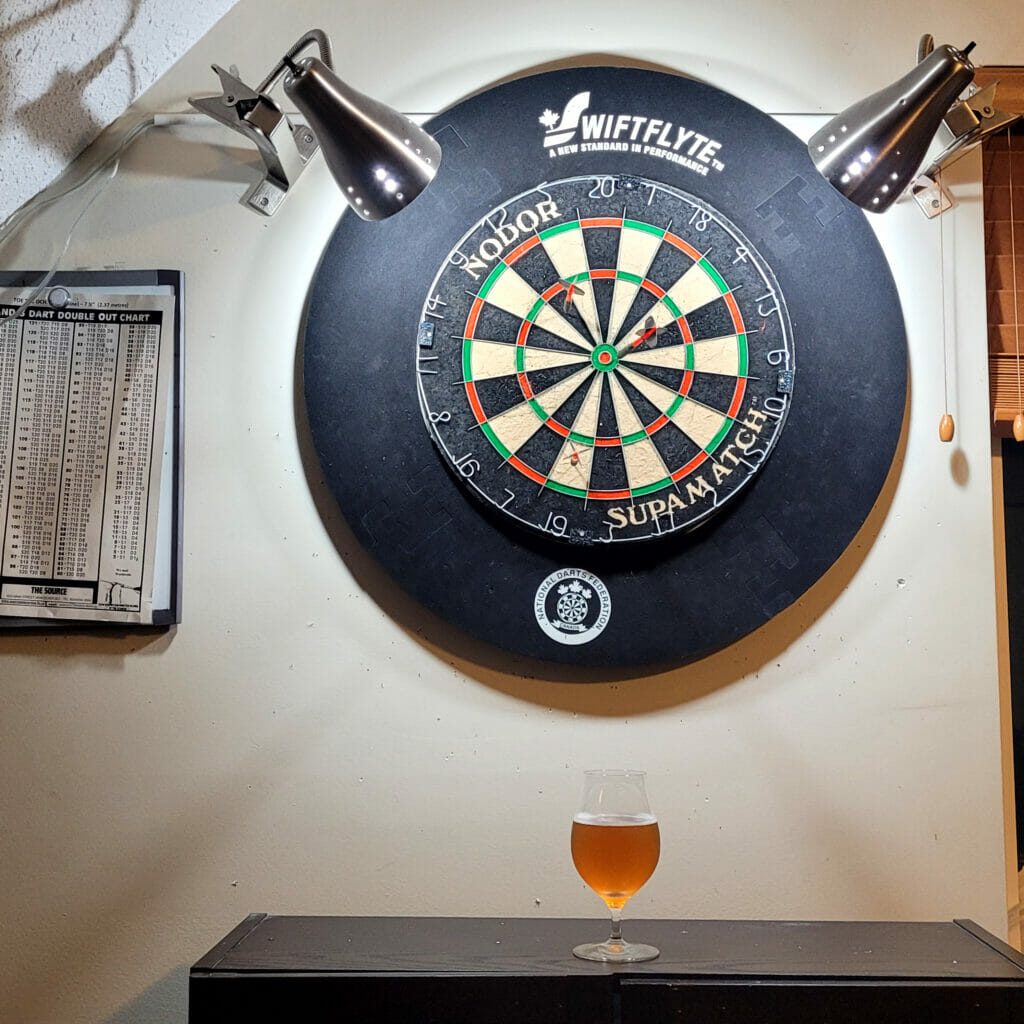 A glass of Angry Hen beer and dart board