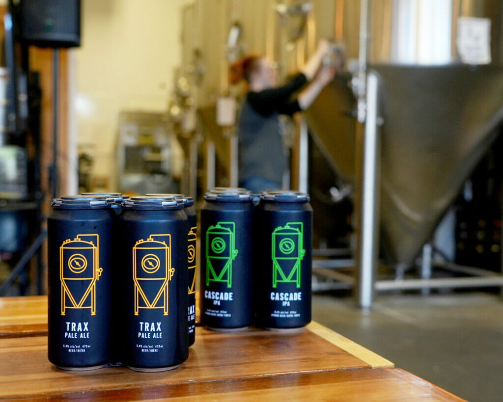 Two four pack of beer with the brewery in the background at Black Kettle Brewing in North Vancouver